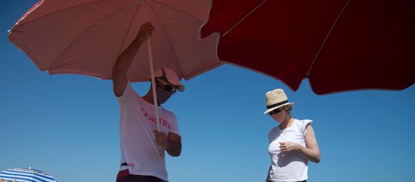Una pareja coloca una sombrilla en una playa de Málaga - Sputnik Mundo