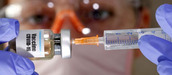 Una mujer sostiene una jeringa médica y un frasco con una etiqueta en la que se lee Vacuna COVID-19 (imagen ilustrativa) - Sputnik Mundo