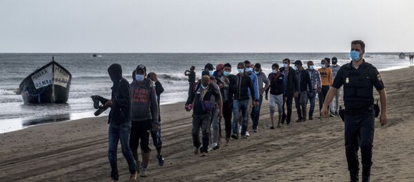 Migrantes de Marruecos caminan por la orilla escoltados por la Policía española tras llegar a la costa de Canarias - Sputnik Mundo