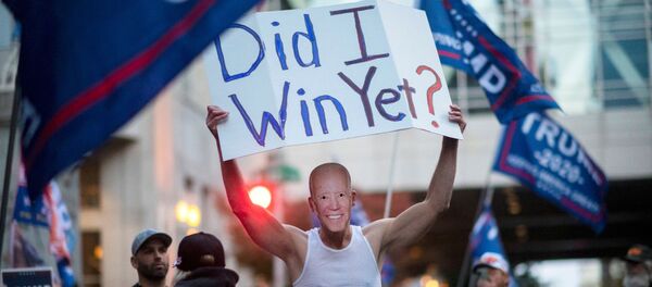 Un partidario de Trump lleva un cartel y una máscara del candidato presidencial demócrata Joe Biden durante una protesta en Filadelfia - Sputnik Mundo