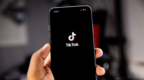 Una persona sostiene un teléfono en el que se ve el logo de TikTok - Sputnik Mundo