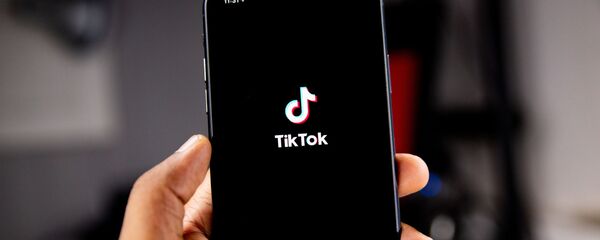 Una persona sostiene un teléfono en el que se ve el logo de TikTok - Sputnik Mundo