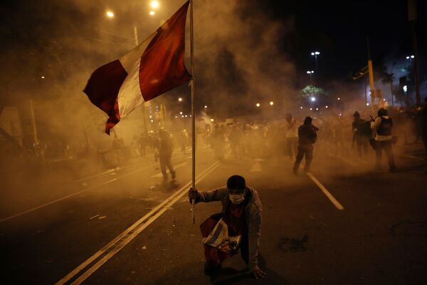 Un manifestante sostiene la bandera de Perú mientras la Policía reprime una protesta contra la destitución de Martín Vizcarra Un manifestante sostiene la bandera de Perú mientras la Policía reprime una protesta contra la destitución de Martín Vizcarra - Sputnik Mundo