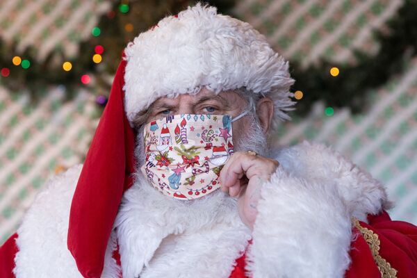 Un hombre personifica a Santa Claus, con su clásica chaqueta roja y un sombrero rojo de campana. Así es como se conoce al mago de la Navidad en la mayoría de los países del mundo. Este año, se añadió una mascarilla a su traje tradicional.En la foto: Santa Claus en un centro comercial de Nueva York. - Sputnik Mundo