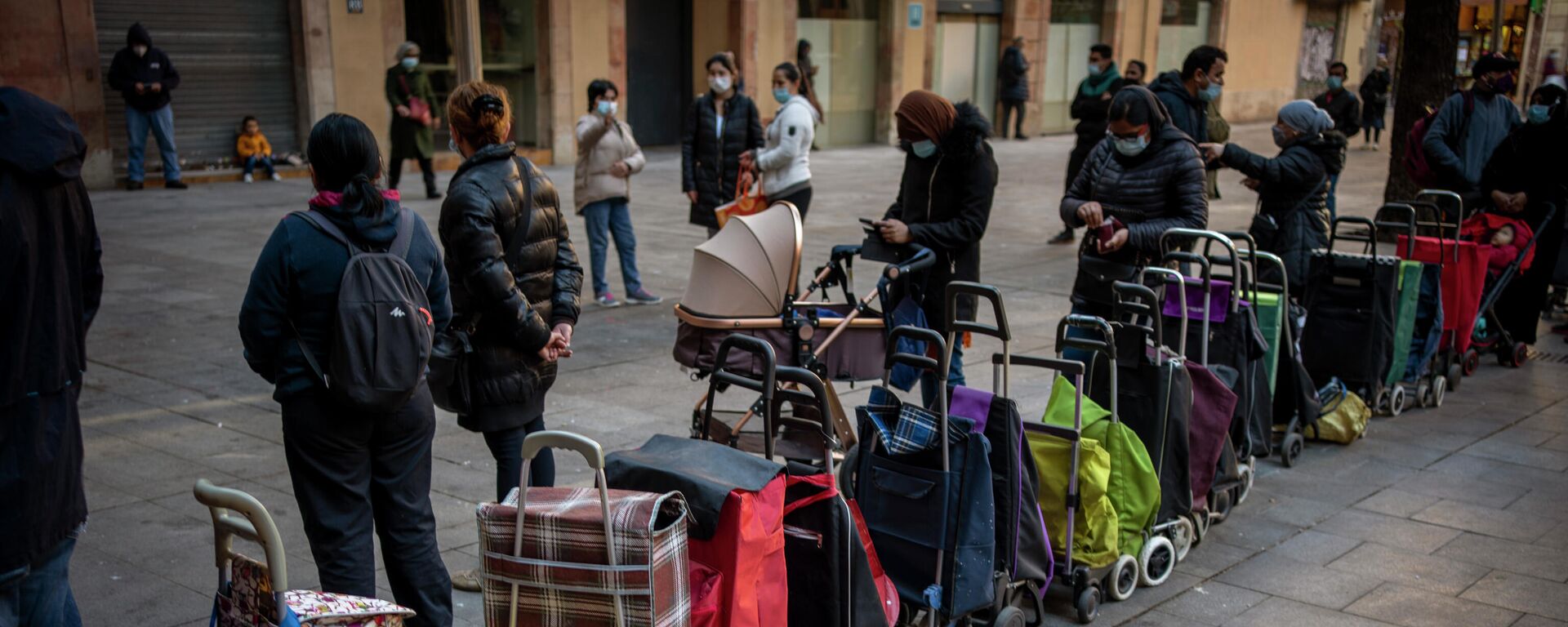 Carritos de compras alineados junto a sus dueños, esperando su turno para recibir un paquete semanal de alimentos y suministros donados, afuera de una iglesia en Barcelona, ​​España, el miércoles 3 de febrero de 2021. - Sputnik Mundo, 1920, 11.11.2023