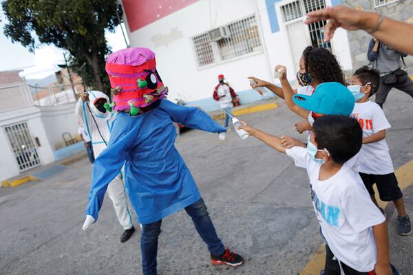 Los niños arrojan alcohol y gel desinfectante de manos contra una persona que lleva una mascarilla que representa el coronavirus durante la quema tradicional de Judas como parte de las celebraciones de Semana Santa en la parroquia de El Cementerio, en Caracas (Venezuela). - Sputnik Mundo