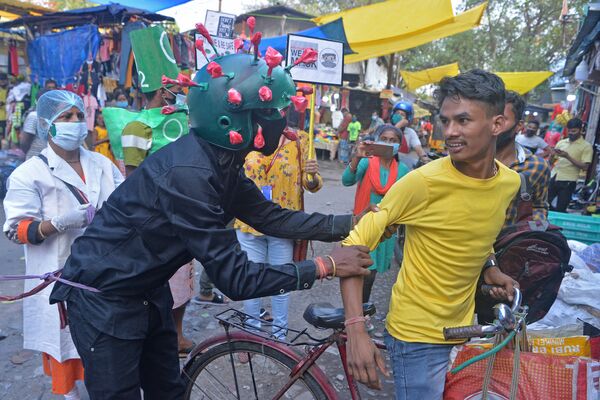 Las dimensiones de la catástrofe no se las esperaban las autoridades indias, quienes en enero del 2021 lanzaron el programa de vacunación en masa más ambicioso del mundo. En la foto: un voluntario explica a los clientes del mercado en la ciudad de Siliguri la necesidad de acatar las normas sanitarias. - Sputnik Mundo