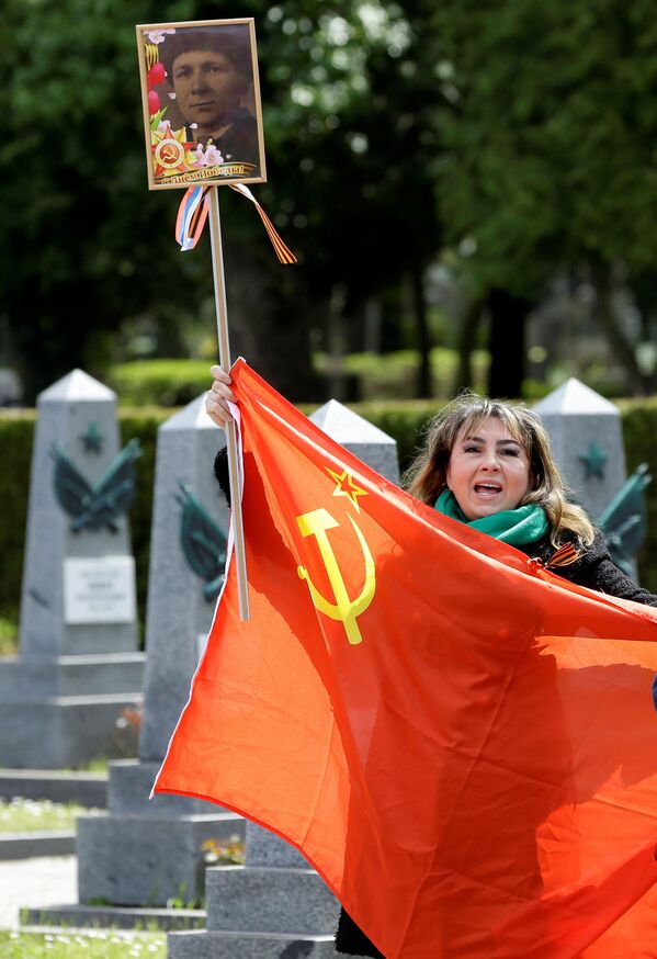 Una mujer sostiene una bandera y canta frente a las tumbas de soldados rusos en el cementerio de Olsany, en la capital de la República Checa, para conmemorar el 76 aniversario del fin de la Segunda Guerra Mundial.   - Sputnik Mundo