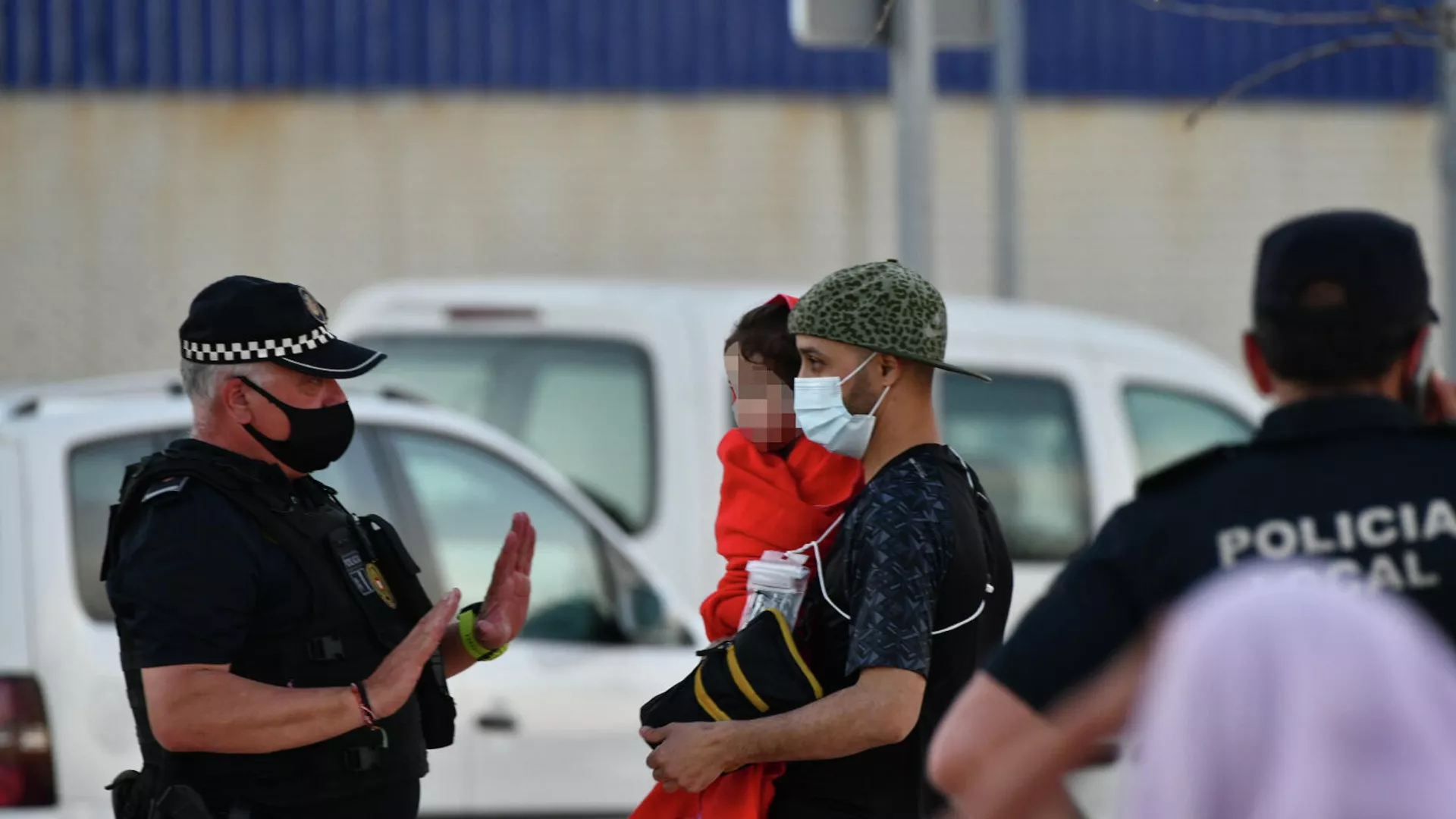 Un policía junto a hombre migrante que coge en brazos a una niña en la playa del Tarajal.