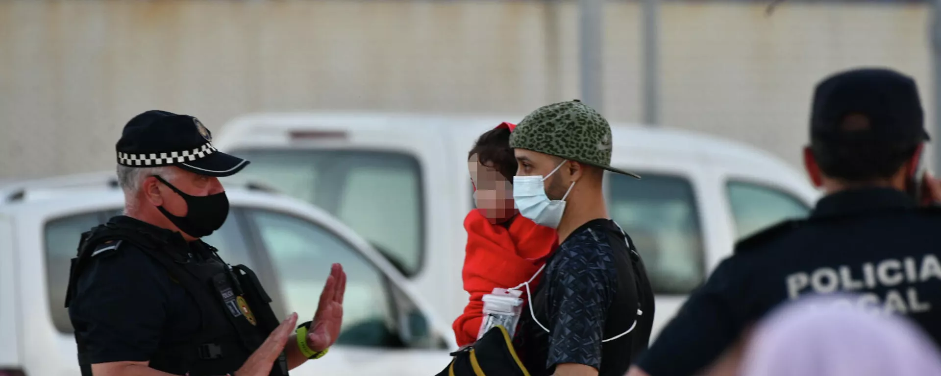 Un policía junto a hombre migrante que coge en brazos a una niña en la playa del Tarajal. Un policía junto a hombre migrante que coge en brazos a una niña en la playa del Tarajal. - Sputnik Mundo, 1920, 18.05.2021