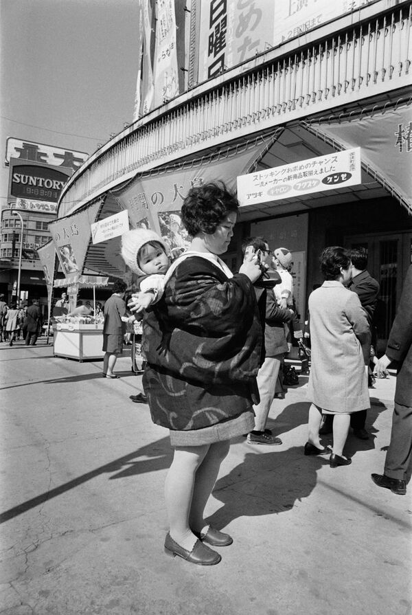 Hoy la mayoría de los teléfonos incorporan una cámara, lo que le permite a las personas registrar cada momento de sus vidas.En la foto: una mujer japonesa con un niño y una cámara en una calle de Tokio en 1972. - Sputnik Mundo