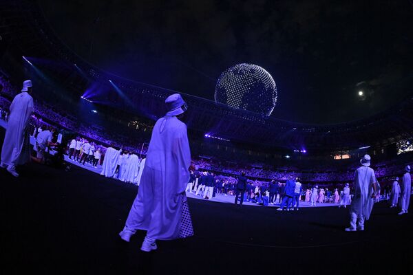 Los atletas y los voluntarios observan cómo los drones vuelan para formar un globo en el cielo sobre el Estadio Olímpico de Tokio. - Sputnik Mundo