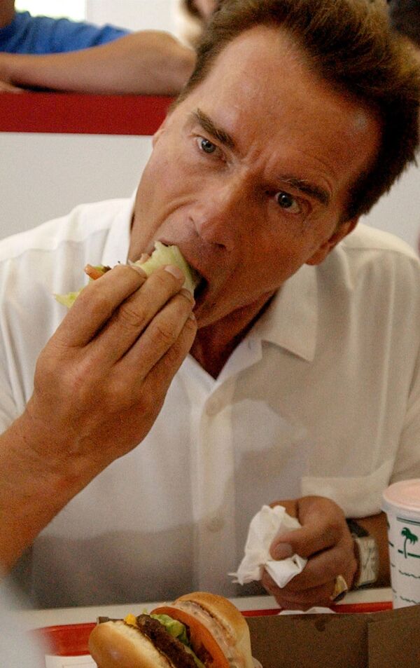 La hamburguesa inició su camino hacia la fama en 1904, tras la Feria Mundial de San Luis (en Missouri). En la foto, el gobernador de California Arnold Schwarzenegger se come una hamburguesa envuelta en lechuga en el In-N-Out Burger de Merced de California en 2003. - Sputnik Mundo