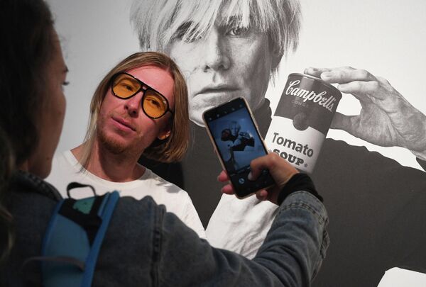 En su testamento, el artista pidió que todo su patrimonio se utilizara para crear una organización para &quot;el avance de las artes visuales&quot;. La Fundación Andy Warhol para las Artes Visuales, establecida en 1987, sigue en funcionamiento hasta hoy.En la foto: una persona posa al lado de un retrato de Andy Warhol en una exposición de sus obras. - Sputnik Mundo