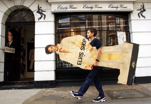 La versión oficial de la causa del fallecimiento del artista ha cambiado con el paso del tiempo, a medida que se realizaron nuevas investigaciones.En la foto: un niño carga una imagen de Elvis Presley a una tienda dedicada al cantante llamada Elvisly Yours en el centro de Londres (Reino Unido) el 16 de agosto de 2002. - Sputnik Mundo