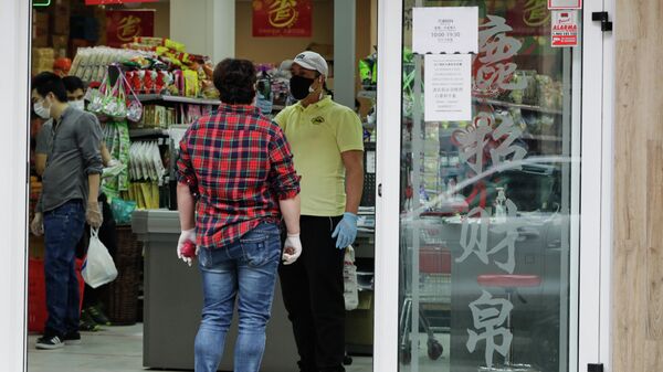 Un trabajador le toma la temperatura a un cliente a la entrada de un supermercado chino abierto en el distrito de Usera el día en el que algunos comercios chinos están volviendo a abrir en Madrid, muchos de ellos en este distrito, conocido como el Chinatown de la capital y donde en algunos casos han comenzado a realizar tomas de temperatura a sus clientes en la entrada, en Madrid (España) a 4 de mayo de 2020. - Sputnik Mundo