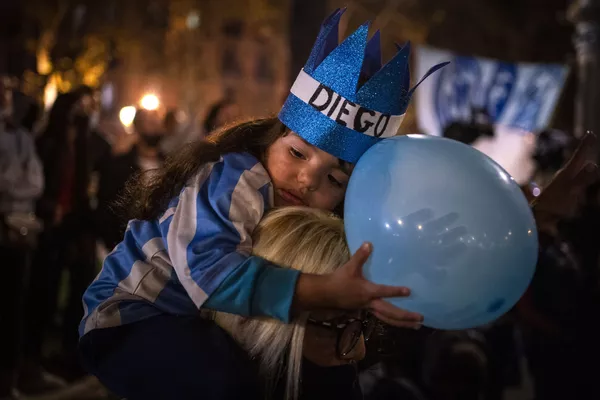 Una niña descansa sobre los hombros de su madre mientras los fanáticos del fútbol conmemoran a la leyenda del fútbol en Barcelona (España), un día después de su fallecimiento, el 26 de noviembre de 2020. Una niña descansa sobre los hombros de su madre mientras los fanáticos del fútbol conmemoran a la leyenda del fútbol en Barcelona (España), un día después de su fallecimiento, el 26 de noviembre de 2020. - Sputnik Mundo