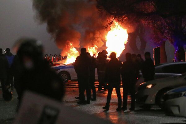 Varias compañías aéreas ya han anunciado retrasos o cancelaciones de vuelos con destino a Kazajistán mientras que el aeropuerto de Almaty había sido tomado por los manifestantes.En la foto: varias personas alrededor de un coche policía en llamas. - Sputnik Mundo