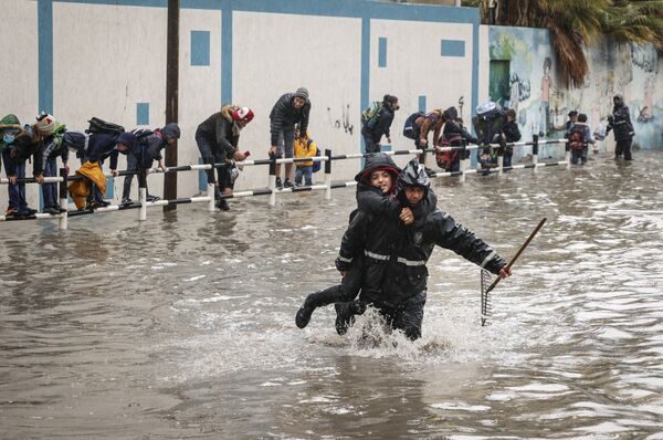 Entre el 14 y 16 de enero, en la Franja de Gaza, muchas zonas quedaron inundadas como resultado de las intensas lluvias, que causaron importantes daños materiales a viviendas y propiedades.En la foto: un empleado municipal ayuda a un estudiante a cruzar una calle inundada en la ciudad de Gaza. - Sputnik Mundo