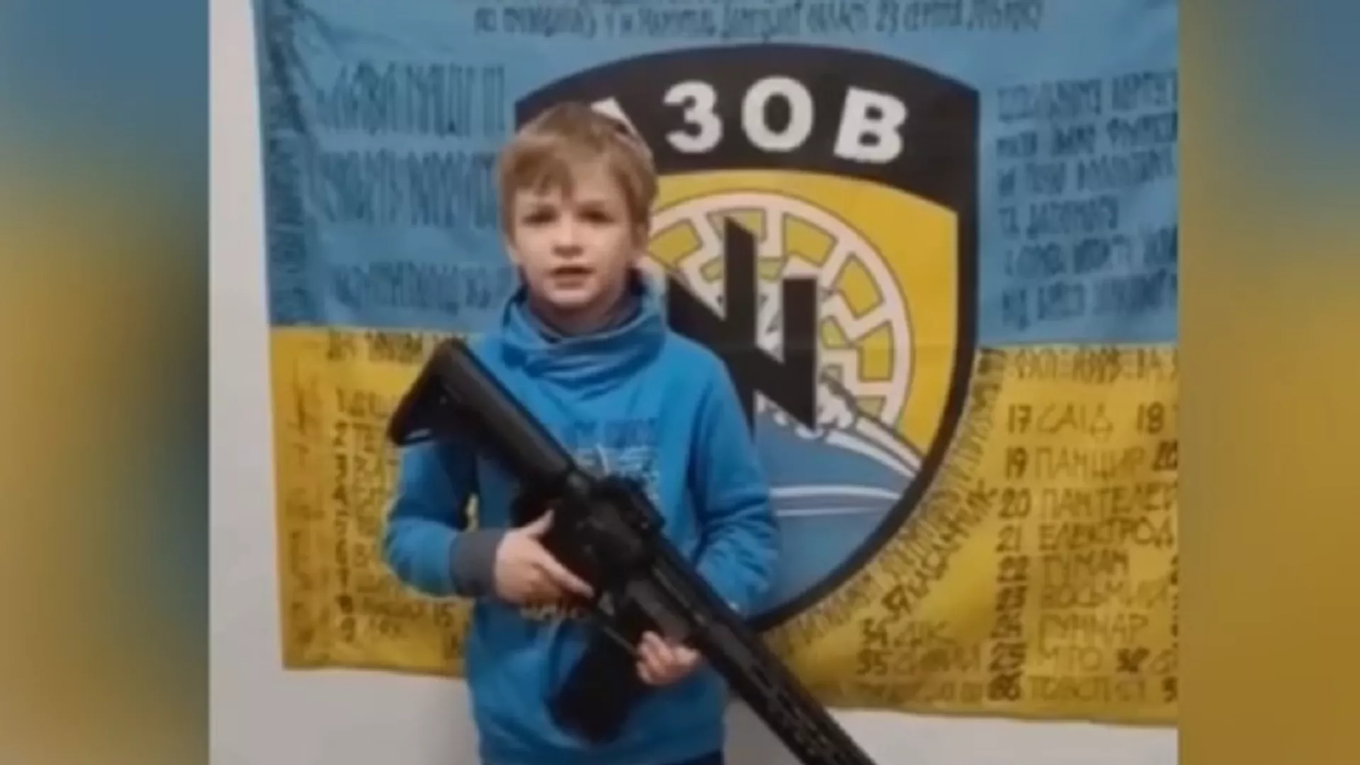 Un niño ucraniano con un fusil posa frente a un símbolo nazi, captura de pantalla