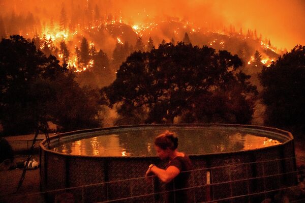 Angela Crawford se apoya en una valla mientras un incendio forestal, llamado McKinney, se devora una ladera por encima de su casa en el Bosque Nacional Klamath, en California, el 30 de julio de 2022. Crawford y su esposo se quedaron, al igual que otros residentes evacuados, para defender su casa del fuego. - Sputnik Mundo