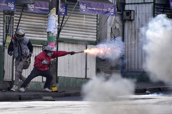 Un manifestante lanza petardos a los policías durante una marcha de protesta de cocaleros en La Paz, Bolivia. 2 de agosto de 2022.Varios centenares de campesinos, agrupados en la Asociación de Productores de Coca (Adepcoca) y opositores al Gobierno del presidente izquierdista, Luis Arce, protestaron en una zona del norte de la ciudad de La Paz para exigir el cierre de un mercado paralelo de comercialización de hoja de coca al que acusan de ser ilegal y de contar con apoyo gubernamental. - Sputnik Mundo