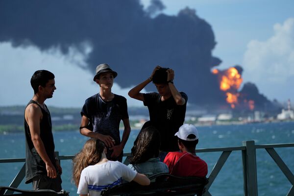 Jóvenes cubanos en el muelle del puerto de Matanzas frente a un tanque de almacenamiento de petróleo en llamas.  - Sputnik Mundo