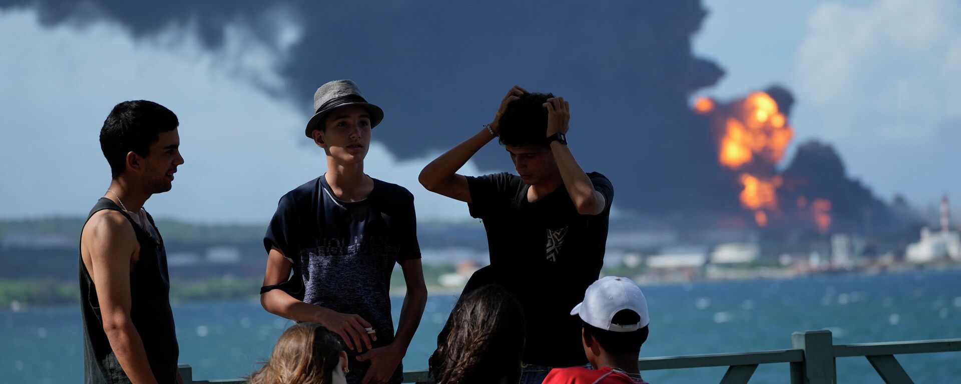 Jóvenes cubanos en el muelle del puerto de Matanzas frente a un tanque de almacenamiento de petróleo en llamas.  - Sputnik Mundo, 1920, 09.08.2022