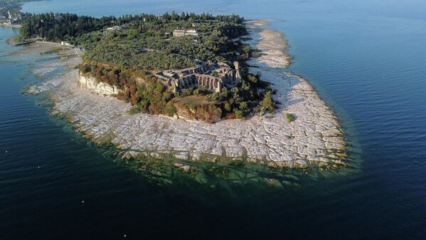 El lecho expuesto del lago de Garda frente a la península de Sirmione, en el norte de Italia. El mayor lago del país ha descendido a mínimos históricos debido a un calor y una sequía sin precedentes. - Sputnik Mundo