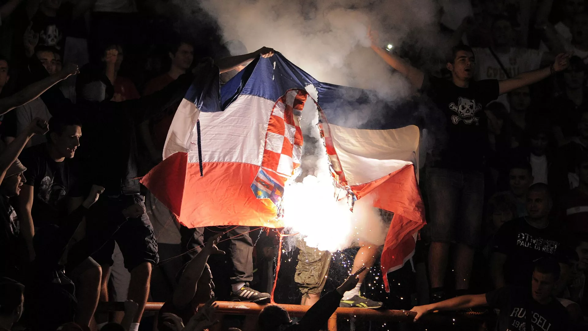 Un grupo de aficionados ultras de Serbia quema una bandera croata durante un partido clasificatorio para el Mundial de Brasil de 2014, en Belgrado