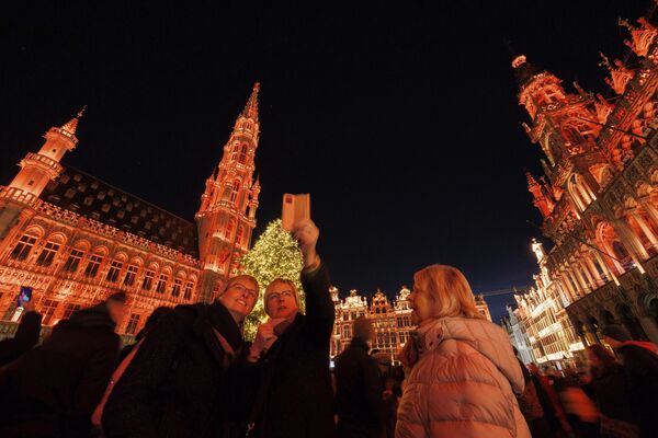 Los visitantes se hacen fotos cerca del árbol de Navidad instalado en la feria navideña de la Grand Place de Bruselas, Bélgica. - Sputnik Mundo