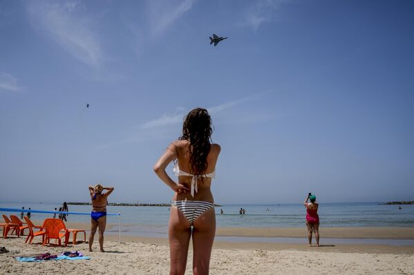 Unos veraneantes observan cómo dos cazas israelíes F-15 sobrevuelan la playa durante un ensayo para un desfile aéreo con motivo del 75 aniversario de la independencia de Israel. Unos veraneantes observan cómo dos cazas israelíes F-15 sobrevuelan la playa durante un ensayo para un desfile aéreo con motivo del 75 aniversario de la independencia de Israel. - Sputnik Mundo