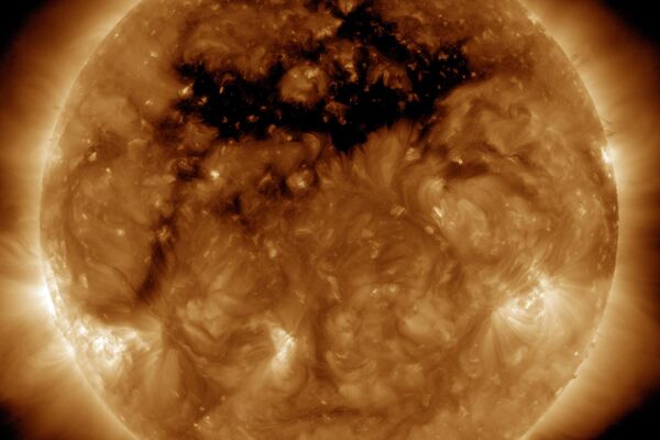 La zona oscura en la parte superior del Sol en esta imagen es un agujero coronal, una región donde el campo magnético está abierto al espacio interplanetario, enviando material coronal a toda velocidad en lo que se llama una corriente de viento solar de alta velocidad. El viento solar de alta velocidad originado en este agujero coronal, y que fotografiado aquí el 10 de octubre de 2015 por el Observatorio de Dinámica Solar de la NASA, creó una tormenta geomagnética cerca de la Tierra que dio lugar a varias noches de auroras. Esta imagen fue tomada en longitudes de onda de 193 Angstroms, que es invisible a nuestros ojos y se colorea típicamente en bronce. - Sputnik Mundo