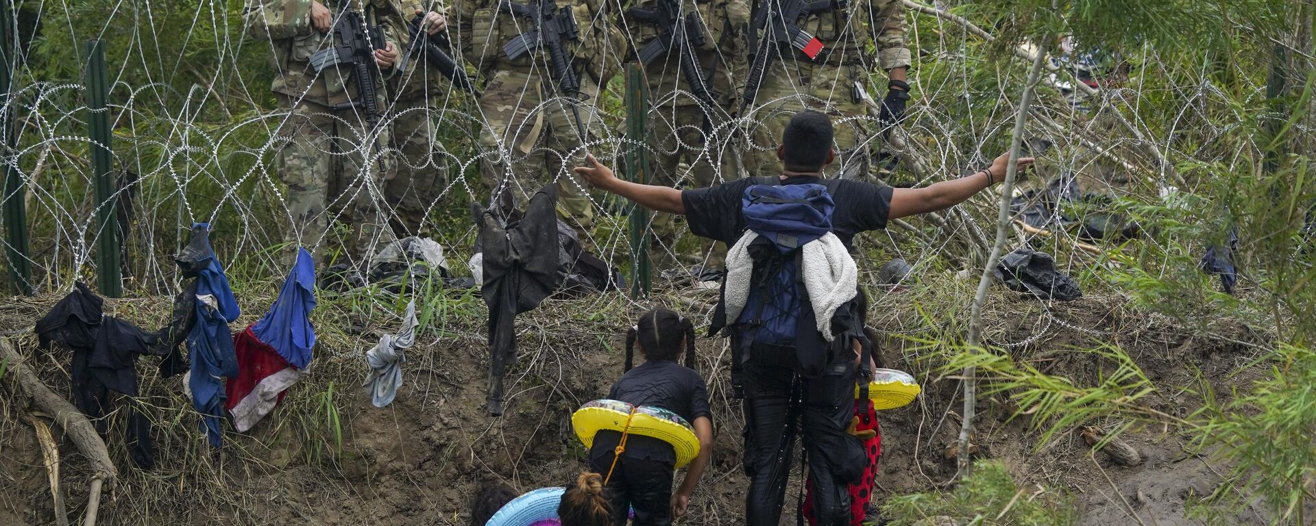 Un migrante hace un gesto a los Guardias Nacionales de Texas que se encuentran detrás de la alambrada en la orilla del río Grande - Sputnik Mundo, 1920, 12.05.2023