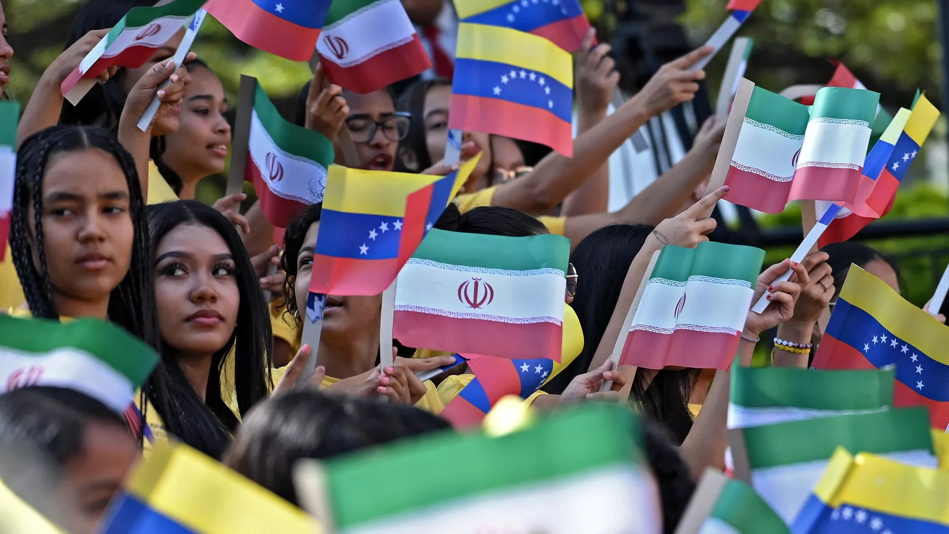 Mujeres jóvenes ondean banderas nacionales de Venezuela e Irán durante la llegada del presidente iraní Ebrahim Raisi al Palacio Presidencial de Miraflores, en Caracas, el 12 de junio de 2023.  