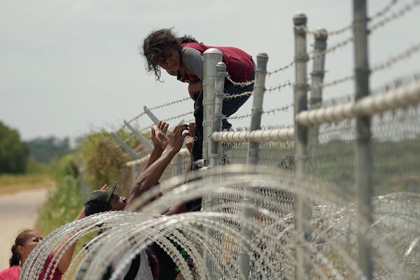 Migrantes, que cruzaron la frontera entre México y Estados Unidos por el Río Grande, suben una valla de alambre de espino en Texas, Estados Unidos. Migrantes, que cruzaron la frontera entre México y Estados Unidos por el Río Grande, suben una valla de alambre de espino en Texas, Estados Unidos. - Sputnik Mundo