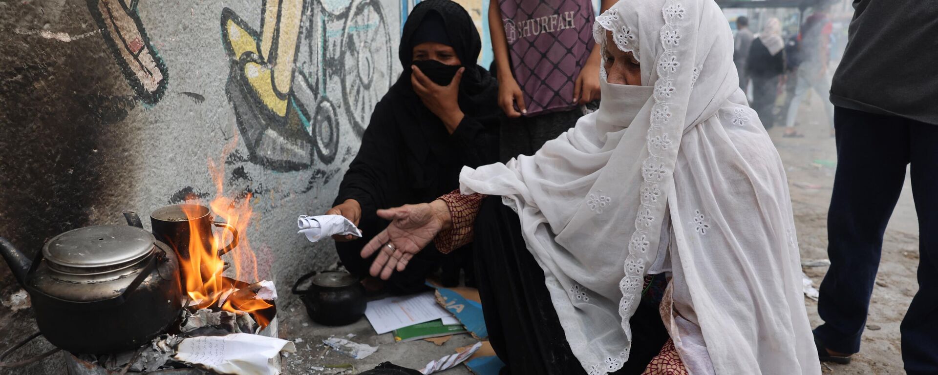 Женщина разжигает бумагой огонь, чтобы нагреть воду для чая, в Рафахе на юге сектора Газа - Sputnik Mundo, 1920, 07.11.2023