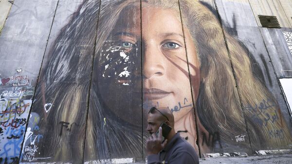 Un hombre pasa junto a una sección de la barrera de separación israelí pintada con un retrato de la palestina Ahed Tamimi, el 6 de noviembre de 2023 en Belén, en la Cisjordania ocupada.  - Sputnik Mundo