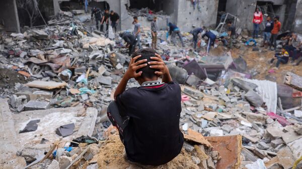 Un niño reacciona mientras la gente rescata pertenencias entre los escombros de un edificio dañado tras los ataques contra Rafah, en el sur de la Franja de Gaza, el 12 de noviembre de 2023  - Sputnik Mundo