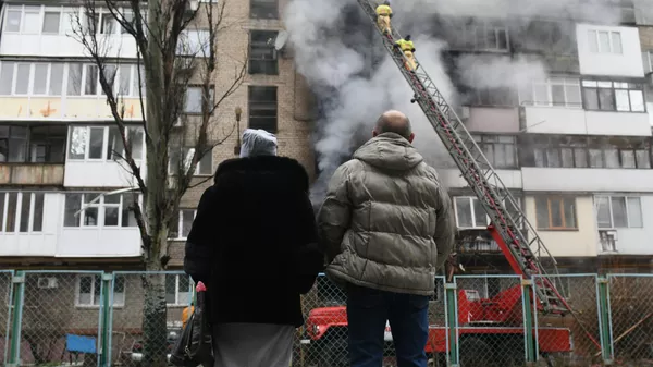 Personas observan cómo bomberos extinguen un incendio en un edificio residencial de Donetsk, provocado por bombardeos de Ucrania. Foto de archivo - Sputnik Mundo