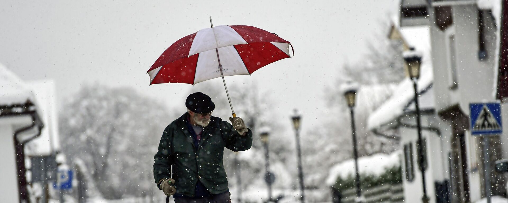 Un hombre se cobija bajo un paraguas mientras camina por una calle cubierta de nieve en Burguete, norte de España, el 16 de enero de 2023  - Sputnik Mundo, 1920, 08.01.2024