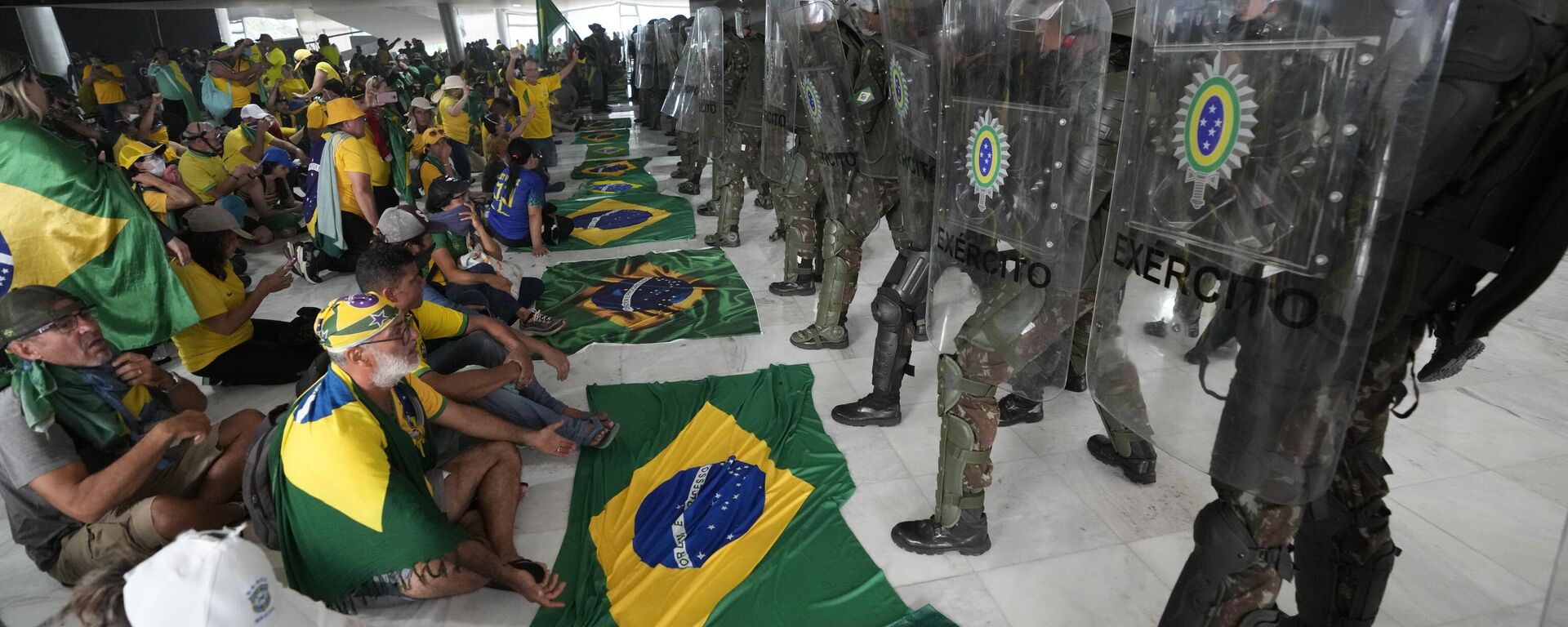 Simpatizantes del expresidente de Brasil, Jair Bolsonaro, se sientan frente a una línea de policías militares dentro del palacio presidencial de Planalto tras irrumpir en el lugar de trabajo oficial del mandatario, en Brasilia, Brasil, el 8 de enero, 2023 - Sputnik Mundo, 1920, 08.01.2024