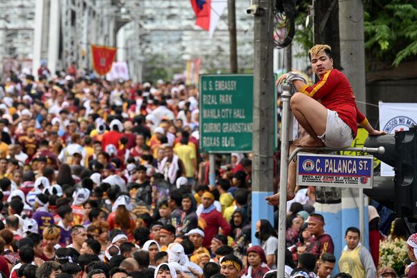 Un devoto católico sube a una señal de tráfico durante la procesión religiosa anual celebrada en honor del llamado Nazareno Negro en Manila, Filipinas. Un devoto católico sube a una señal de tráfico durante la procesión religiosa anual celebrada en honor del llamado Nazareno Negro en Manila, Filipinas. - Sputnik Mundo