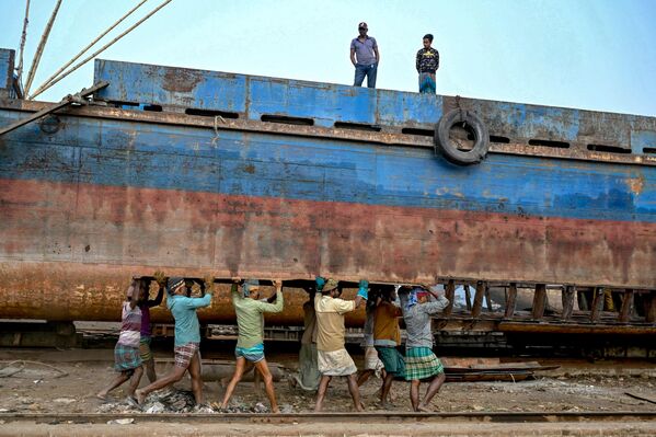 Trabajadores transportando una plancha de metal para reparar un viejo barco en un astillero a orillas del río Buriganga en Daka, Bangladesh. Trabajadores transportando una plancha de metal para reparar un viejo barco en un astillero a orillas del río Buriganga en Daka, Bangladesh. - Sputnik Mundo