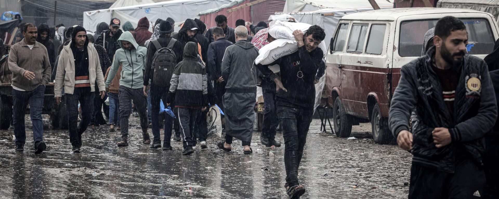 Palestinos caminan bajo la lluvia en un campamento improvisado que alberga a palestinos desplazados, en Rafah - Sputnik Mundo, 1920, 14.01.2024