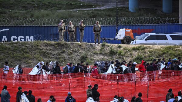 Agentes de aduanas y protección fronteriza hacen guardia mientras los inmigrantes esperan a ser procesados en un centro de tránsito de la Patrulla Fronteriza de Estados Unidos después de cruzar la frontera desde México en Eagle Pass, Texas, el 22 de diciembre de 2023. - Sputnik Mundo