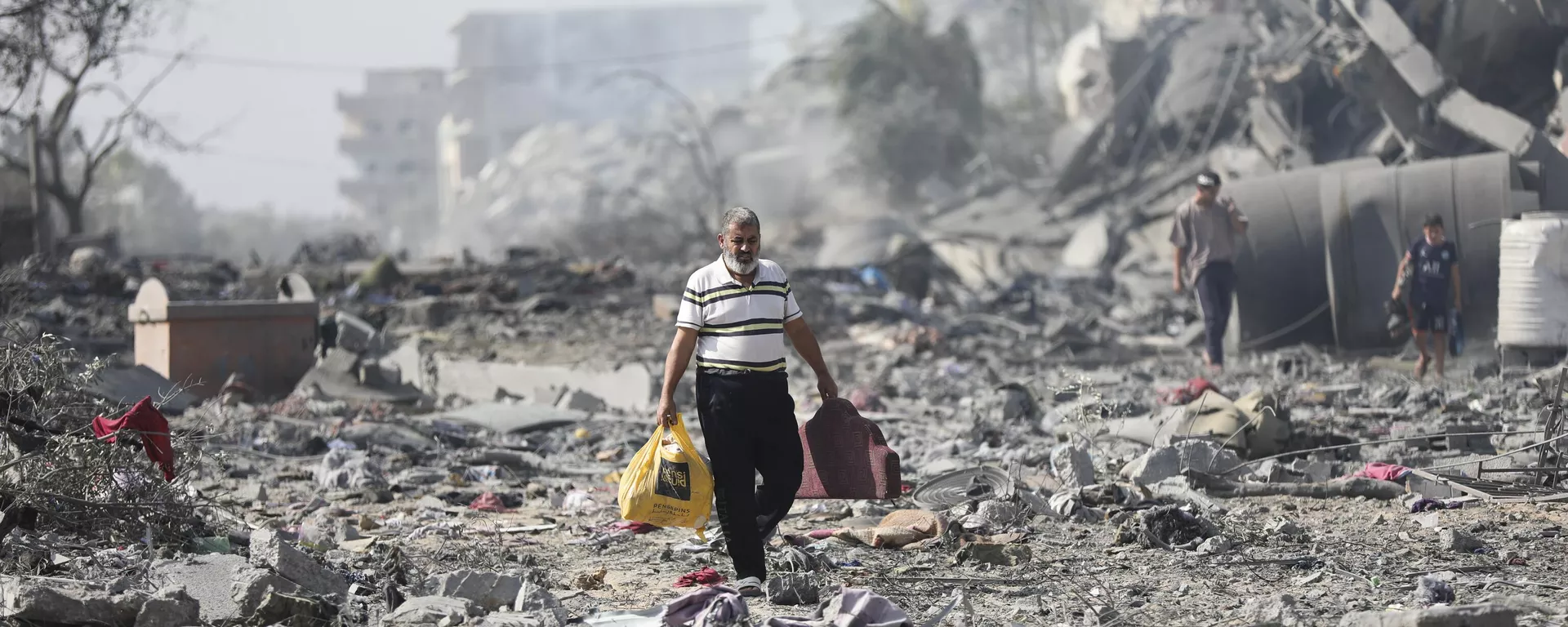 Palestinos caminan junto a los edificios destruidos en el bombardeo israelí sobre al-Zahra, en las afueras de la ciudad de Gaza, el 20 de octubre de 2023 Palestinos caminan junto a los edificios destruidos en el bombardeo israelí sobre al-Zahra, en las afueras de la ciudad de Gaza, el 20 de octubre de 2023 - Sputnik Mundo, 1920, 07.02.2024