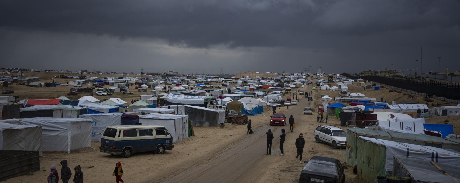 Palestinos desplazados por la ofensiva israelí en la Franja de Gaza caminan por un campamento improvisado de tiendas de campaña en Rafah  - Sputnik Mundo, 1920, 12.02.2024