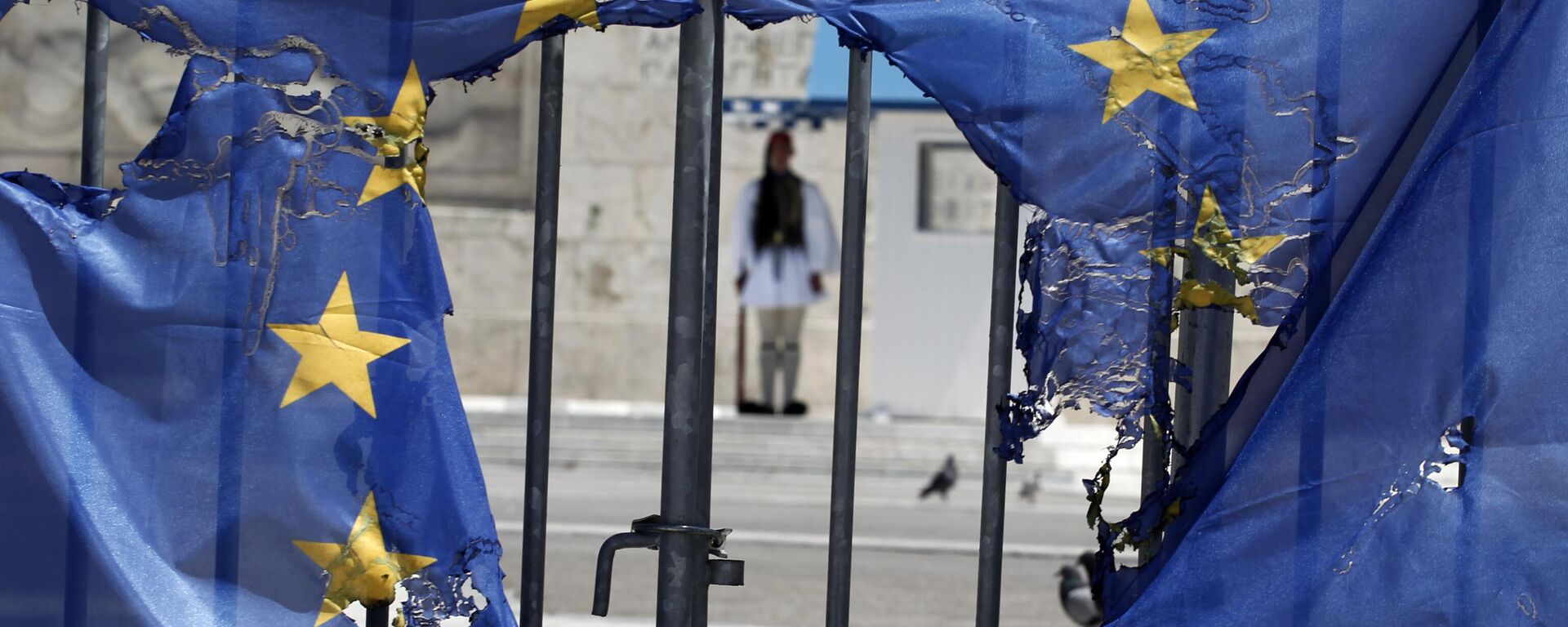 Un guardia presidencial griego permanece enmarcado por los restos de una bandera de la Unión Europea, medio quemada por manifestantes en Atenas, el 1 de mayo de 2013 - Sputnik Mundo, 1920, 17.07.2024