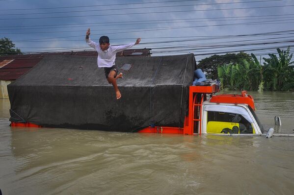 Un niño salta a las aguas que inundaron una carretera debido a las fuertes lluvias y al desbordamiento de un río, en Demak, provincia de Java Central, Indonesia. - Sputnik Mundo